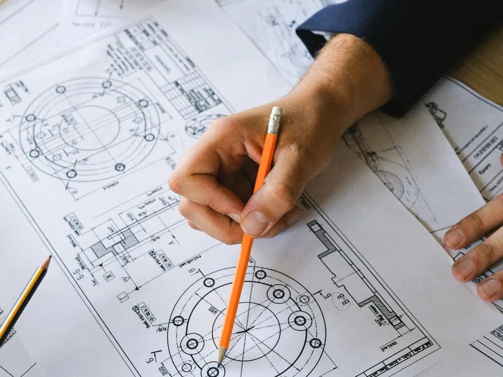 Hand marking a technical drawing with an orange pencil