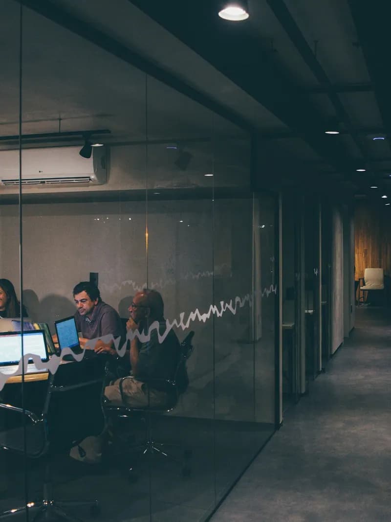Team working at computers in a dark glass-walled office