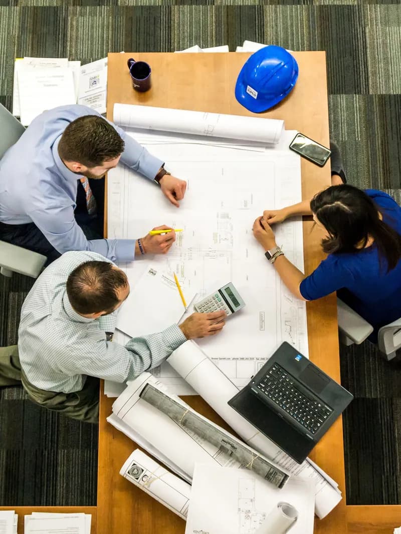Team reviewing plans beside a hard hat on a table, seen from above
